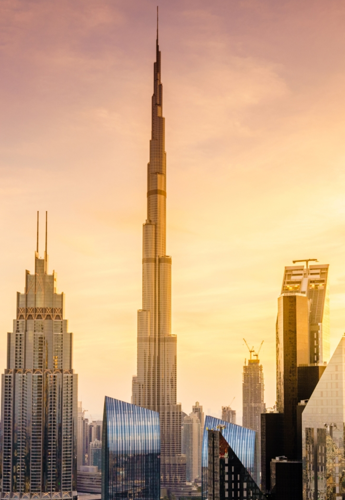 The Burj Khalifa and surrounding modern skyscrapers silhouetted against a warm, golden sunset sky, highlighting Dubai's impressive skyline.