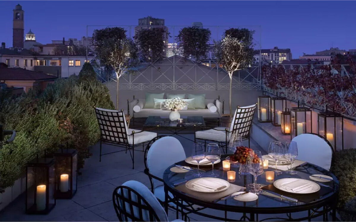 An intimate rooftop terrace at night, decorated with candles, greenery, and cozy seating, offering a serene ambiance with views of the city skyline.